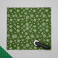 Winter Solstice II Green Snowflakes Metallic quilting cotton by Jason Yenter for In The Beginning Fabrics — fabric flat lay showing tossed white snowflakes and gold metallic star dots on deep forest green ground, shown with cutting mat and rotary cutter. Quilt blocks shown for inspiration. Coordinating fabrics and quilt patterns are available at IraRobi Quilts.