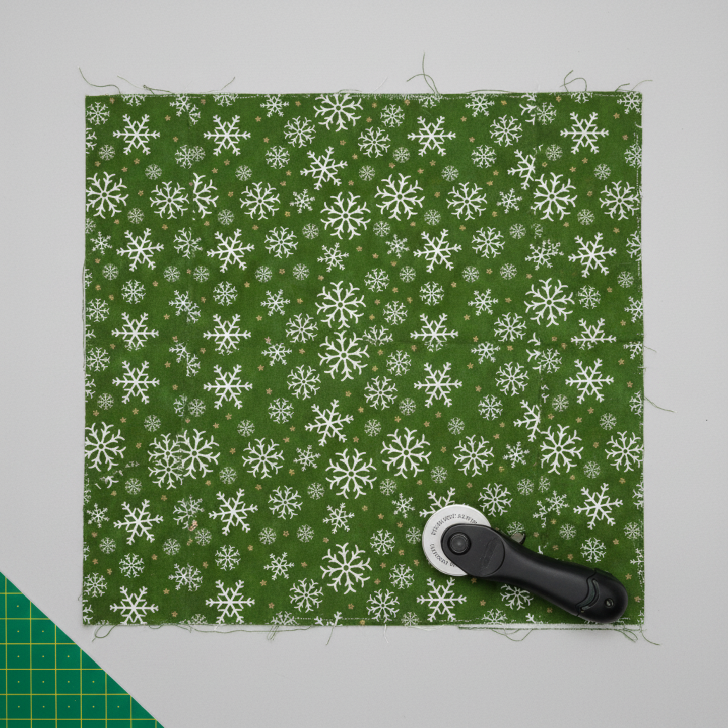 Winter Solstice II Green Snowflakes Metallic quilting cotton by Jason Yenter for In The Beginning Fabrics — fabric flat lay showing tossed white snowflakes and gold metallic star dots on deep forest green ground, shown with cutting mat and rotary cutter. Quilt blocks shown for inspiration. Coordinating fabrics and quilt patterns are available at IraRobi Quilts.