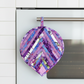 Leaf-Shaped Quilted Hot Pad – Purple Garden hanging upside down on a stainless steel oven handle, pointed tip down, loop hooked over the bar, showing herringbone chevron strip piecing in purple, lavender, blue, pink, magenta, and floral botanical prints – handmade by IraRobi Quilts