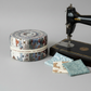 High Meadow Farm Jelly Roll by Lynette Anderson beside a vintage sewing machine with coordinating fabric swatches on grey background