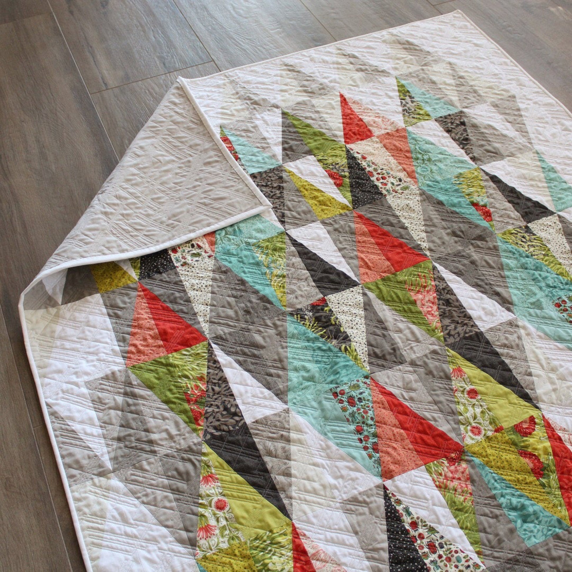 Harlequin quilt pattern by Robin Pickens – full quilt with colorful diamond design displayed on a wooden floor