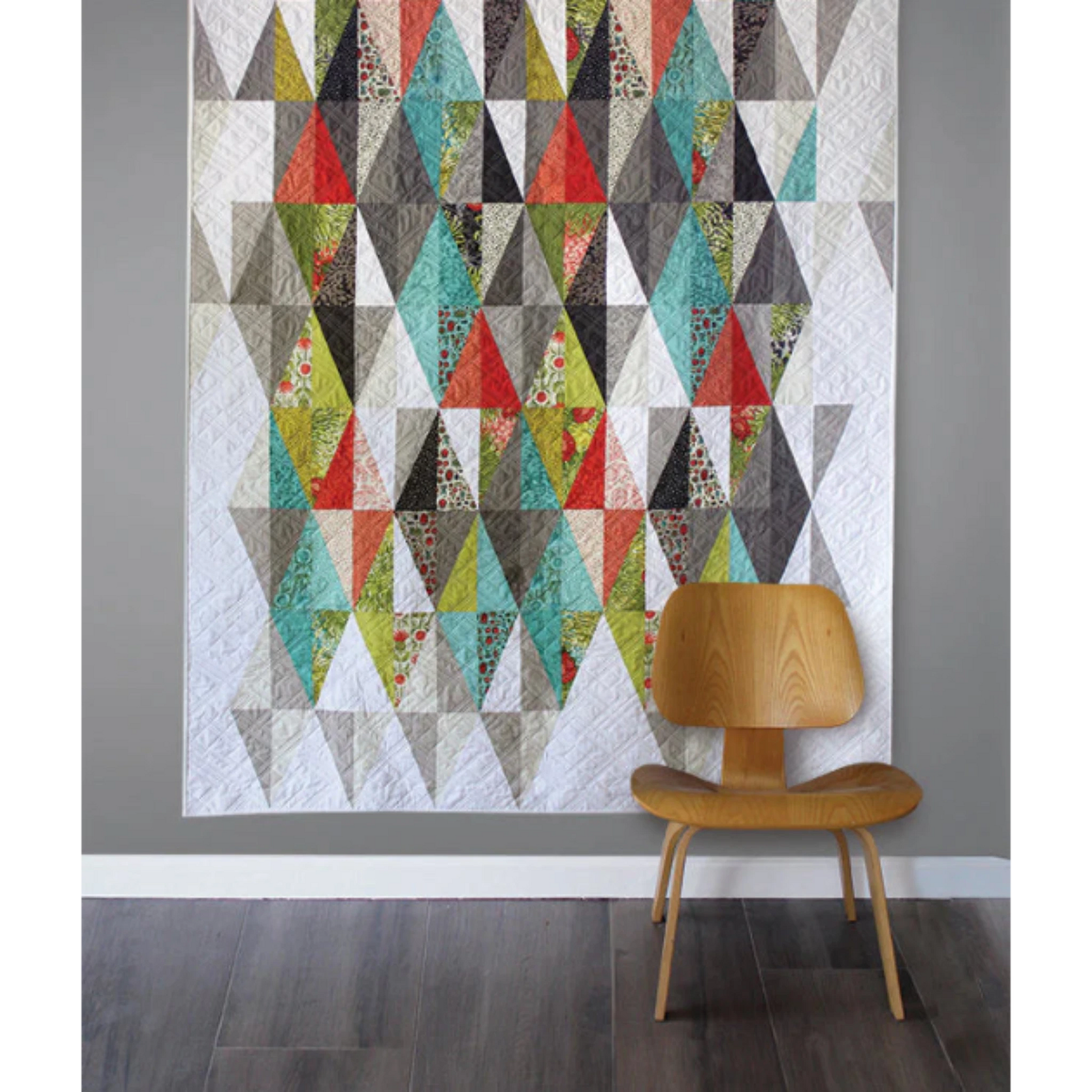 Harlequin quilt pattern by Robin Pickens – colorful geometric diamond quilt displayed on a wall with wooden chair