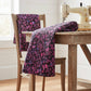 Halcyon II Magenta Vines fabric draped over rustic wood chair and rolled on farmhouse table beside vintage sewing machine, magenta and pink botanical on black cotton by Jason Yenter for In The Beginning Fabrics