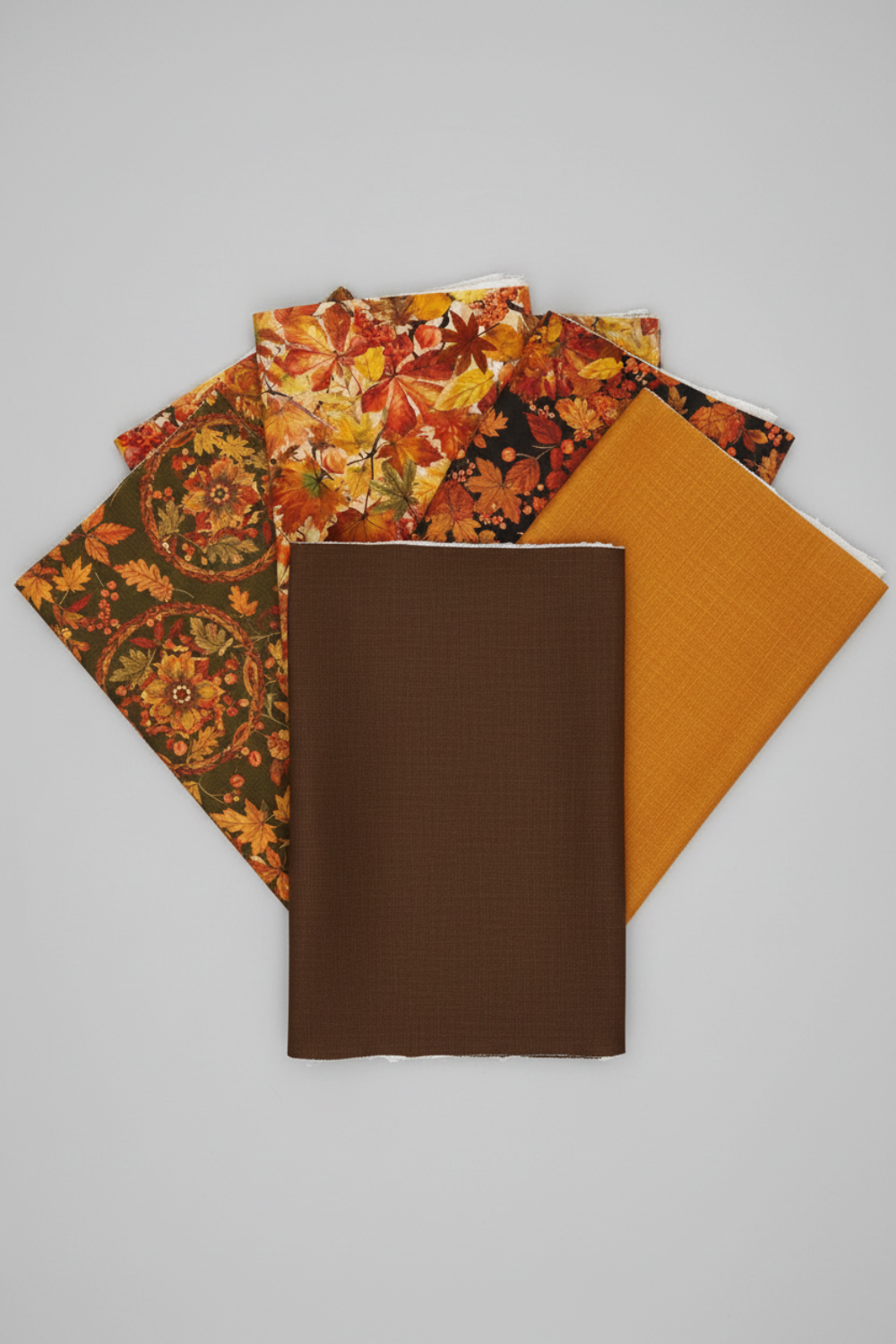 Interwoven Brown Fabric by Jason Yenter for In The Beginning Fabrics stacked with coordinating autumn fabrics – medallion leaves, packed autumn leaves, dense leaves and berries, and golden-amber crosshatch. Perfect for fall and Thanksgiving quilts. Shop at IraRobi Quilts | #brownfabric #interwoven #autumnquilt #fallquilt #quiltingfabric #fabricstack #thanksgivingquilt
