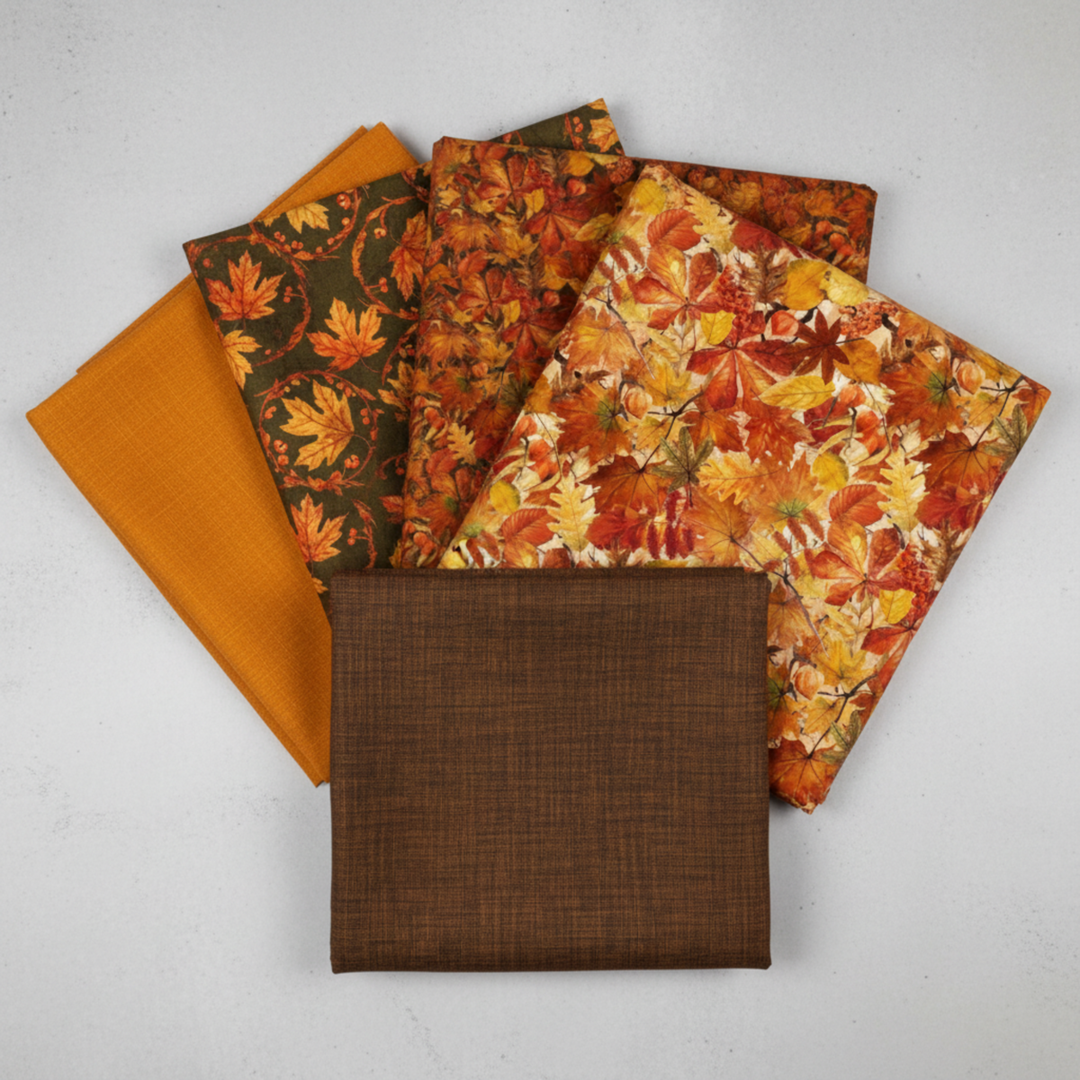 Interwoven Brown Fabric by Jason Yenter for In The Beginning Fabrics fanned with coordinating autumn fabrics – medallion leaves print, packed autumn leaves print, dense leaves and berries print, and golden-amber crosshatch texture