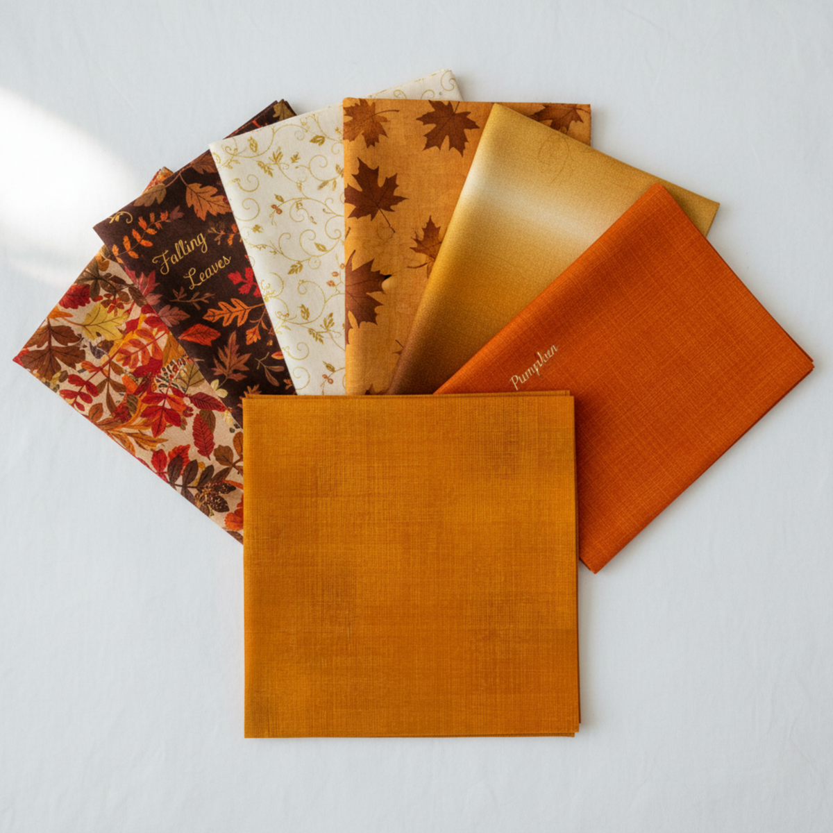 Interwoven Butterscotch Fabric by Jason Yenter for In The Beginning Fabrics as the hero fabric in a warm fall coordination fan — golden amber crosshatch tonal prominently in front, with coordinating autumn prints fanned behind. 100% cotton, 43–44" wide.