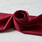 Interwoven Cherry Fabric by Jason Yenter for In The Beginning Fabrics draped in an elegant spiral fold on a white surface — deep cherry red crosshatch tonal blender with linen-like texture depth and rich burgundy-wine tonal variation. 100% cotton quilting cotton.
