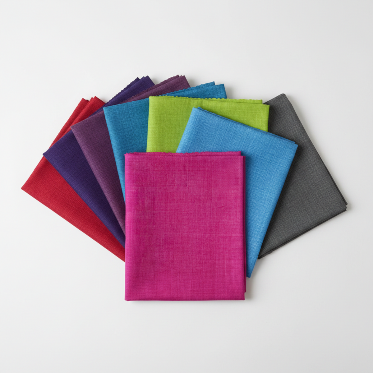 Interwoven Hot Pink Fabric by Jason Yenter for In The Beginning Fabrics fanned alongside coordinating colorways — all sharing the same fine crosshatch texture print in vivid saturated tones. Versatile tonal blenders for modern and rainbow quilts. 100% cotton, 43–44" wide.