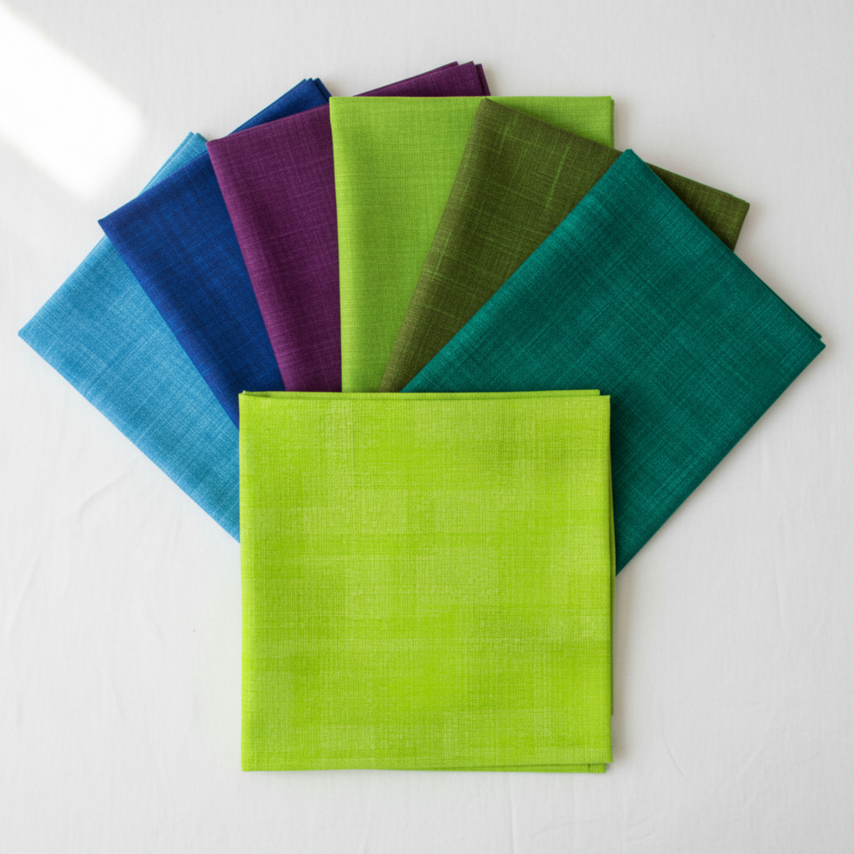 Interwoven Lime Fabric by Jason Yenter for In The Beginning Fabrics as the hero fabric in an Interwoven rainbow coordination fan — vivid lime green crosshatch tonal prominently in front, with coordinating quilting cotton tonals fanned behind. 100% cotton, 43–44" wide.