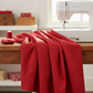 Interwoven Red Fabric by Jason Yenter for In The Beginning Fabrics cascading in generous folds beside a white sewing machine — vivid true red crosshatch tonal blender with linen-like depth. Perfect for modern, scrappy, and rainbow quilts. Available at IraRobi Quilts.