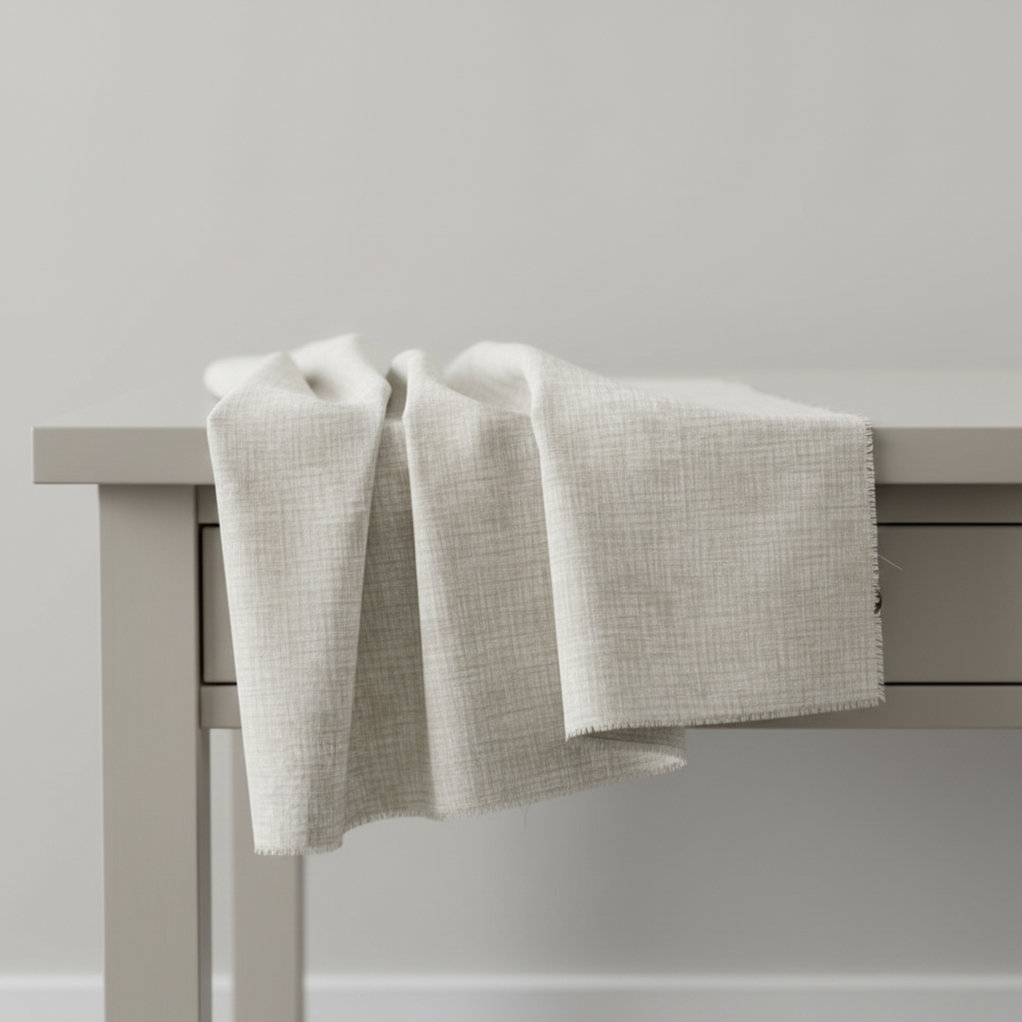 Interwoven Taupe Fabric by Jason Yenter for In The Beginning Fabrics — soft cream and taupe linen-look crosshatch blender quilting cotton draped over a grey table edge in a clean studio setting, raw cut edges visible, 100% cotton, 43–44" wide