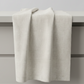 Interwoven Taupe Fabric by Jason Yenter for In The Beginning Fabrics — soft cream and taupe linen-look crosshatch blender quilting cotton draped vertically over a grey table edge in a clean quilting studio, raw cut edges, 100% cotton, 43–44" wide