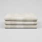 Interwoven Taupe Fabric by Jason Yenter for In The Beginning Fabrics — soft cream and taupe linen-look crosshatch blender quilting cotton neatly folded showing pattern detail, raw cut edges, light grey background, 100% cotton, 43–44" wide