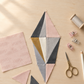Unfinished Jewels quilt block on a sewing table beside a pale blush Celestial Washi Rose Quartz fabric remnant, thread, scissors, and sewing clips. Quilts shown for inspiration feature the Jewels Quilt Pattern by Zen Chic — all available at IraRobi Quilts.