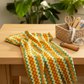 Jungle Friends Multi Stripe 3-yard cut fabric displayed on a sewing table in a warm sewing room, showing orange, green, yellow, white, and gold geometric stripes.
