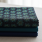 La Luna Black Bursts fabric by Jason Yenter for In The Beginning Fabrics folded in a stack on a light linen surface with coordinating deep teal and navy fabrics – allover geometric star burst blender with glowing hexagonal dots in teal, aqua, and chartreuse on deep black, perfect for celestial and night-themed quilt projects, 100% cotton, 3 yard cut