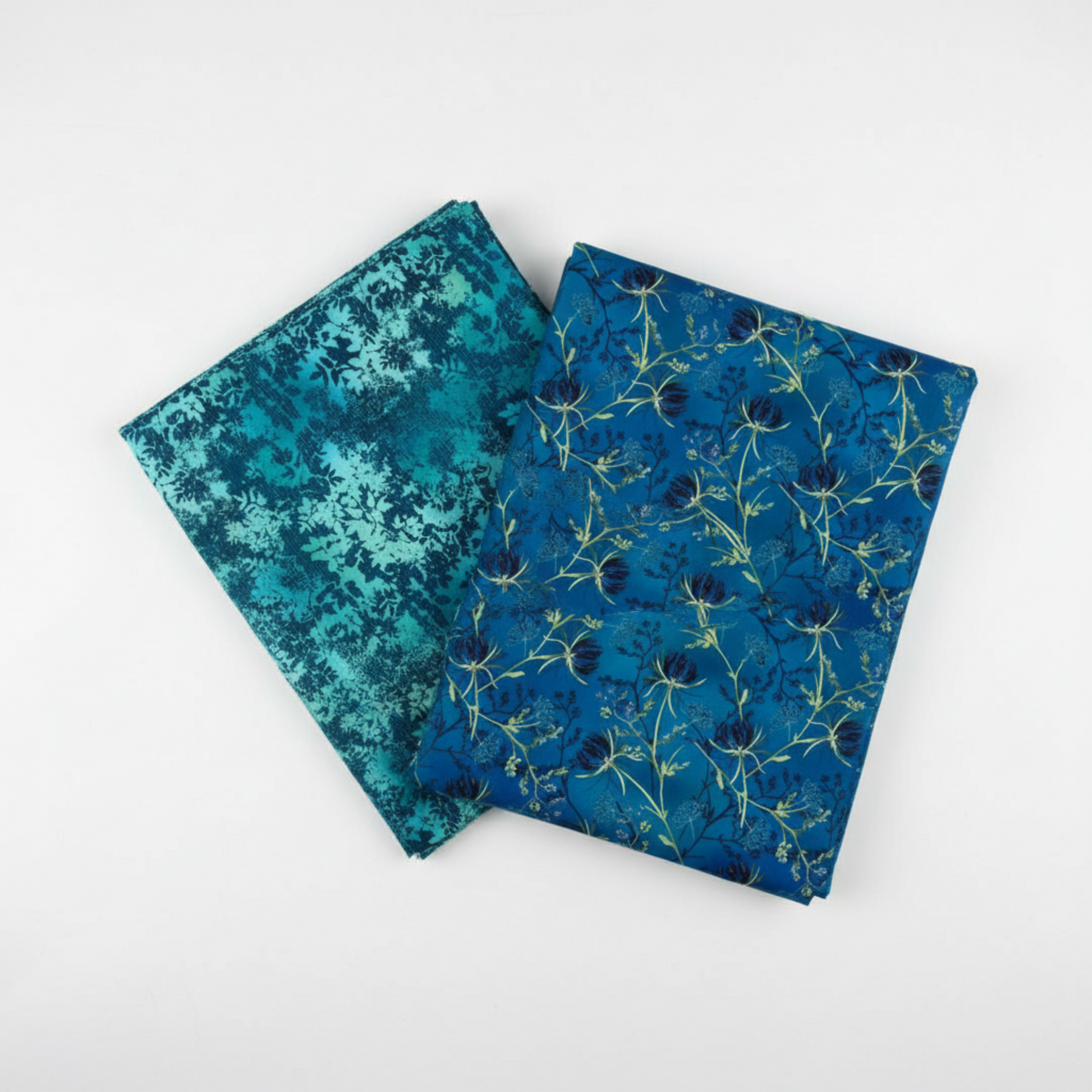 La Luna Blue Night Blooms and La Luna Teal Leaves quilting cotton fabrics by Jason Yenter for In The Beginning Fabrics shown in a coordinate fan – allover trailing botanical with navy moonflower blooms and chartreuse stems fanned with dense tonal leaf silhouette print, both on rich cobalt watercolor wash, 100% cotton, 3 yard cuts