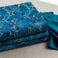 La Luna Blue Night Blooms fabric by Jason Yenter for In The Beginning Fabrics folded in a stack on a light linen surface with coordinating deep teal and navy fabrics – allover trailing botanical with navy moonflower blooms and chartreuse stems on rich cobalt watercolor wash, perfect for night garden quilt projects, 100% cotton, 3 yard cut