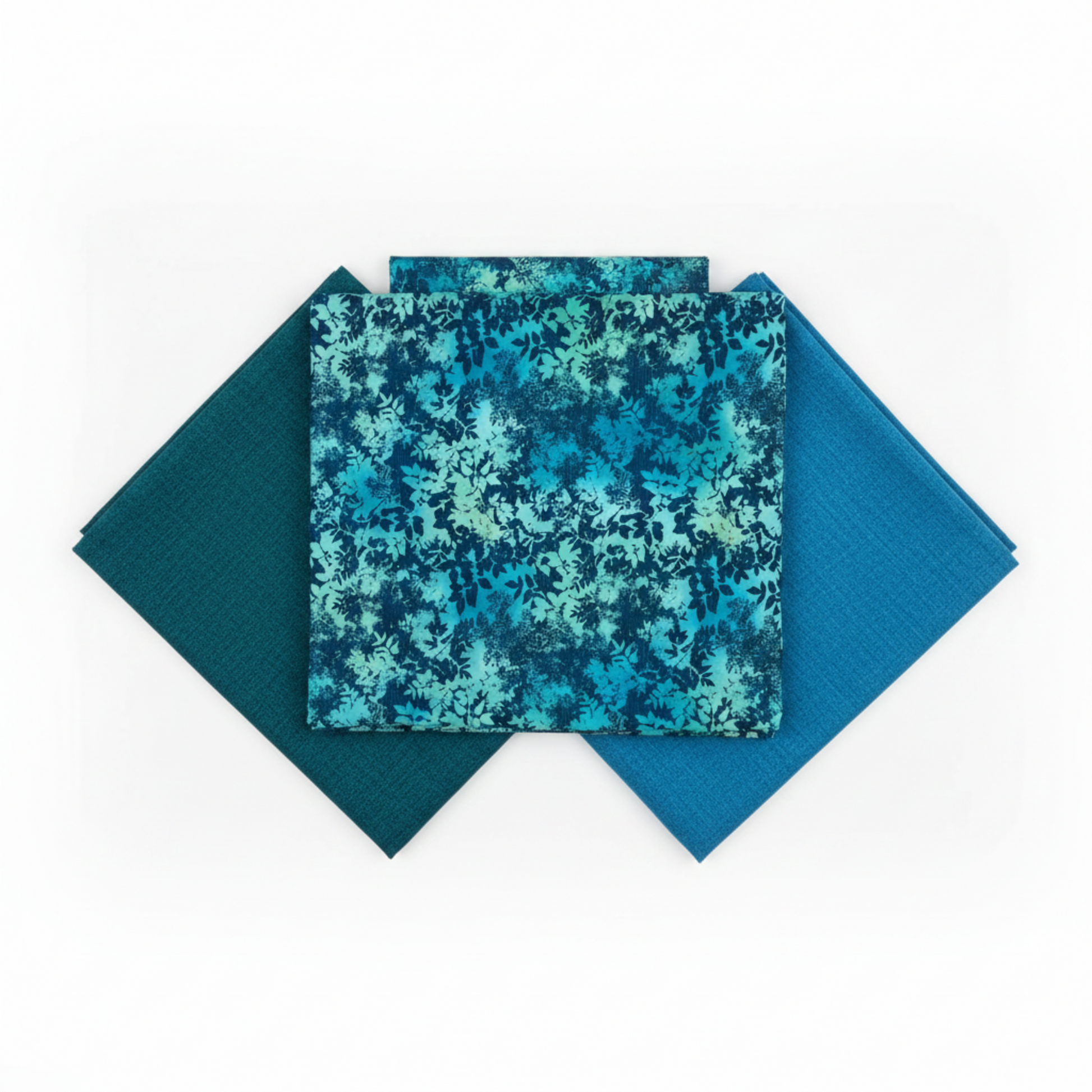 La Luna Teal Leaves quilting cotton fabric by Jason Yenter for In The Beginning Fabrics shown in a coordinate fan with Interwoven Dark Teal and Interwoven Ocean blenders – dense allover tonal leaf silhouette print in aqua, teal, chartreuse, and deep navy on rich cobalt watercolor wash, 100% cotton, 3 yard cut