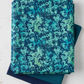 La Luna Teal Leaves fabric by Jason Yenter for In The Beginning Fabrics folded in a stack on a light linen surface with coordinating deep teal and navy fabrics – dense allover tonal leaf silhouette print with fern fronds and botanical sprigs in aqua, teal, chartreuse, and navy on rich cobalt watercolor wash, perfect for night garden quilt projects, 100% cotton, 3 yard cut