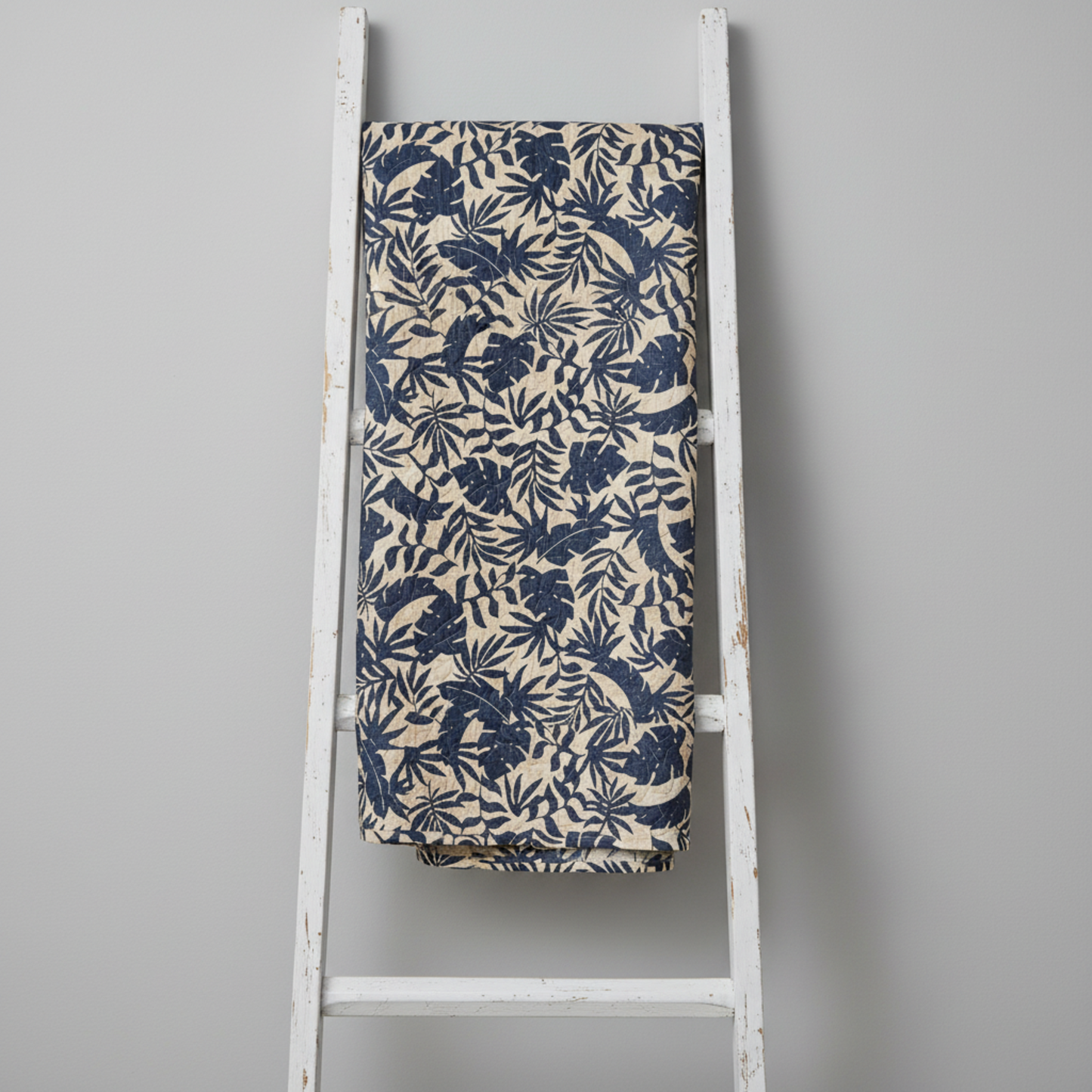 Breezeway Textured Palms Blue/Cream quilting cotton by Maywood Studio — fabric draped over a weathered white wooden ladder showing natural drape and bold navy-blue tropical palm and monstera silhouette print