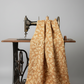 Front Porch by Dolores Smith, Swing Rust for Marcus Fabrics — rust-amber quilting cotton with cream scrolling acanthus leaf motif draped over a vintage sewing machine, 100% cotton 43–44" wide