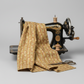 Front Porch Railings Gold quilting cotton by Dolores Smith for Marcus Fabrics — fabric draped over a vintage antique sewing machine showing natural drape and olive-gold leaf garland stripe print