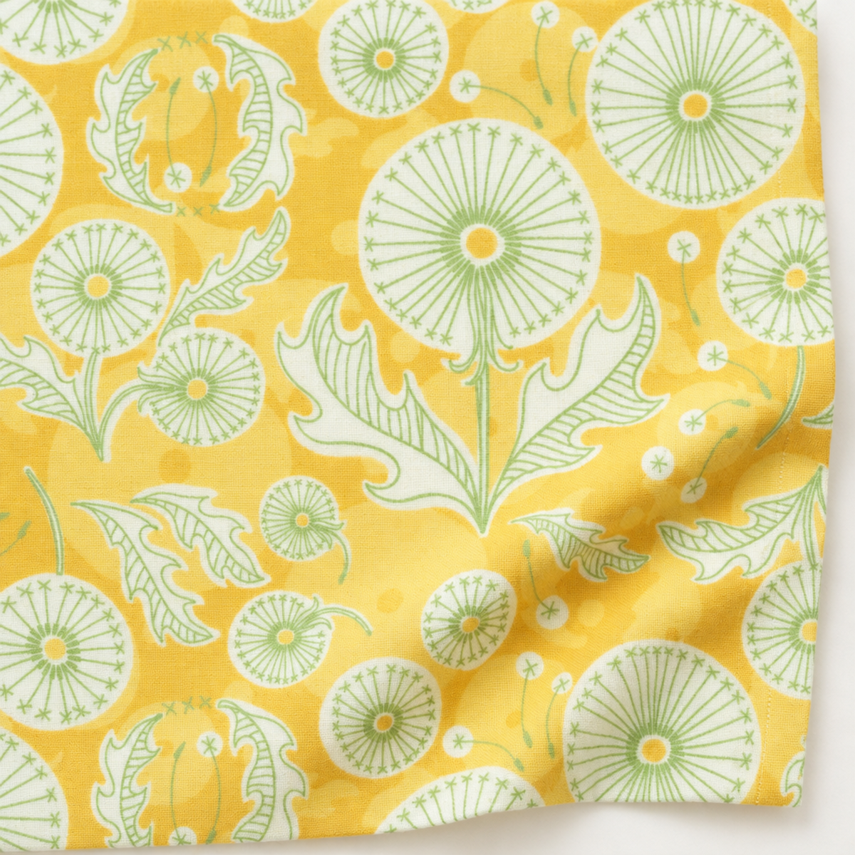 Dandi Duo Dandi Toile Maize fabric laid flat, showing dandelion seed heads, leaves, and scattered seeds on golden yellow.
