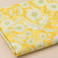 Folded Dandi Duo Dandi Toile Maize fabric showing pale-green dandelion seed heads on a golden-yellow ground.