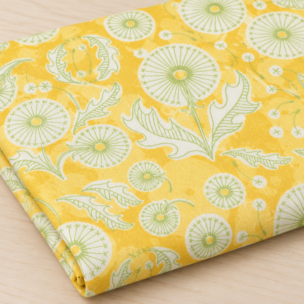 Folded Dandi Duo Dandi Toile Maize fabric showing pale-green dandelion seed heads on a golden-yellow ground.