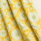 Folds of Dandi Duo Dandi Toile Maize fabric showing pale-green dandelion seed heads and leaves on a golden-yellow ground.