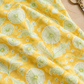 Dandi Duo Dandi Toile Maize fabric draped on a sewing table beside thread and scissors.