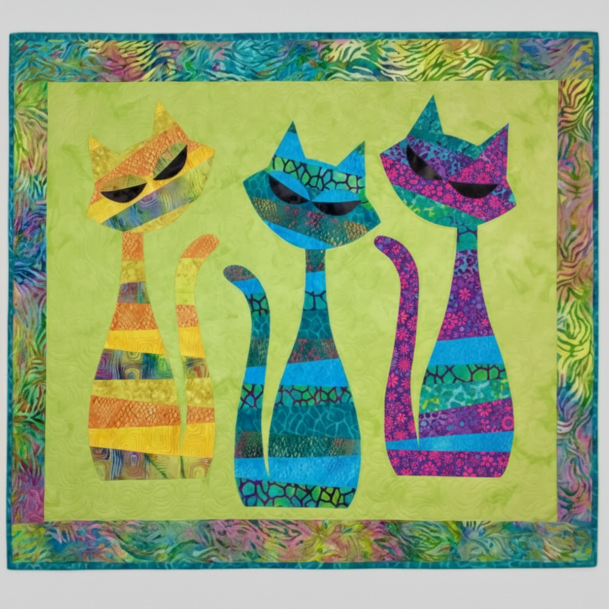 PAWsitivity Purple Field quilting cotton by Jason Yenter for In The Beginning Fabrics — shown as the purple cat appliqué fabric in the ModCat Quilt Pattern by Colourwerx, alongside coordinating yellow-orange and teal-blue batik cats on a chartreuse background with a multicolor batik border. Quilts shown for inspiration feature the ModCat Quilt Pattern by Colourwerx — available at IraRobi Quilts.