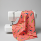Coral sorbet pink quilting cotton with colorful tropical parrots draped over a modern white sewing machine — Safari Fun Jungle Birds Sorbet by Terry Runyan for Benartex