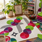 nterwoven Spring Grass Fabric by Jason Yenter for In The Beginning Fabrics featured in curved circle blocks in a Moon Dance quilt top on a wooden sewing table — paired with hot pink, teal, purple, and red coordinating prints on a white background. Fabric stack, wonder clips bowl, rotary cutter, and potted plant in the scene. Quilts shown for inspiration feature the Moon Dance Quilt Pattern by Sew Kind of Wonderful — available at IraRobi Quilts.