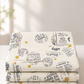 Folded stack of Celestial News Dropping Moonbeam fabric by Zen Chic for Moda Fabrics, featuring charcoal newsprint motifs and mustard-gold dots on ivory.