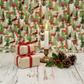 Winter Solstice II Multi Deer Metallic quilting cotton by Jason Yenter for In The Beginning Fabrics — fabric draped as a festive backdrop with wrapped Christmas gifts, pine cones, holly sprig, and a glowing brass candle holder in an elegant holiday vignette. Quilt blocks shown for inspiration. Coordinating fabrics and quilt patterns are available at IraRobi Quilts.