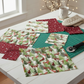 Winter Solstice II Multi Deer Metallic quilting cotton by Jason Yenter for In The Beginning Fabrics — fabric cut into large squares alongside coordinating burgundy snowflake and cream metallic fabrics in a holiday quilt in progress, with cutting mat and rotary cutter in a cozy workspace. Quilts shown for inspiration. Coordinating fabrics and quilt patterns are available at IraRobi Quilts.