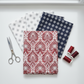 Nature's Winter Red Snowflake Ogee quilting cotton by Jason Yenter for In The Beginning Fabrics — flat lay hero fanned with coordinating winter fabrics, silver scissors, and deep red thread spools on a white surface. Coordinating fabrics and quilt patterns available at IraRobi Quilts.