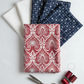 Nature's Winter Red Snowflake Ogee quilting cotton by Jason Yenter for In The Beginning Fabrics — vertical flat lay as hero fanned with coordinating winter fabrics, silver scissors, and deep red thread spools on a white surface. Coordinating fabrics and quilt patterns available at IraRobi Quilts.