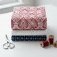 Nature's Winter Red Snowflake Ogee quilting cotton by Jason Yenter for In The Beginning Fabrics — vertical flat lay folded as hero on a tall coordinating fabric stack with silver scissors and deep red thread spools on a white surface. Coordinating fabrics and quilt patterns available at IraRobi Quilts.