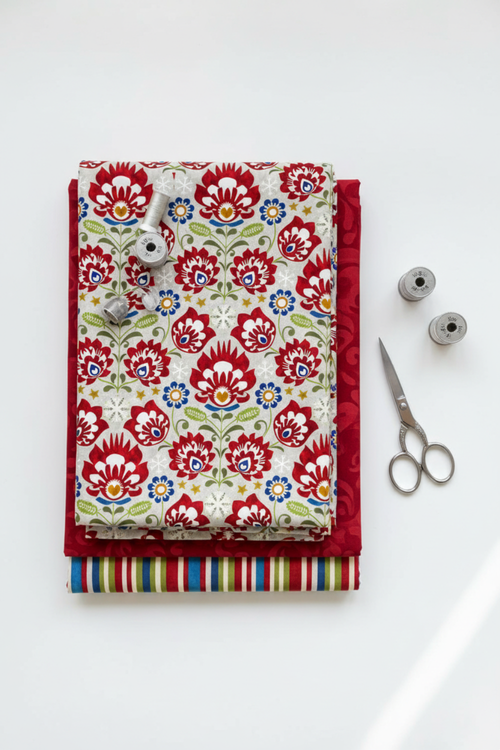 NYSNO New Snow Multicolor Floral quilting cotton by Jason Yenter for In The Beginning Fabrics — vertical flat lay folded as hero on a coordinating fabric stack with silver scissors and thread spools on a white surface. Coordinating fabrics and quilt patterns available at IraRobi Quilts.