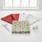 NYSNO New Snow Multicolor Garland quilting cotton by Jason Yenter for In The Beginning Fabrics — flat lay hero with coordinating Red Swirl and White Snowflakes fabrics fanned behind, silver scissors and thread spools on white surface. Coordinating fabrics and quilt patterns available at IraRobi Quilts.