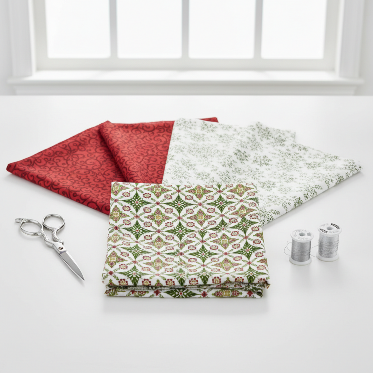 NYSNO New Snow Multicolor Garland quilting cotton by Jason Yenter for In The Beginning Fabrics — flat lay hero with coordinating Red Swirl and White Snowflakes fabrics fanned behind, silver scissors and thread spools on white surface. Coordinating fabrics and quilt patterns available at IraRobi Quilts.