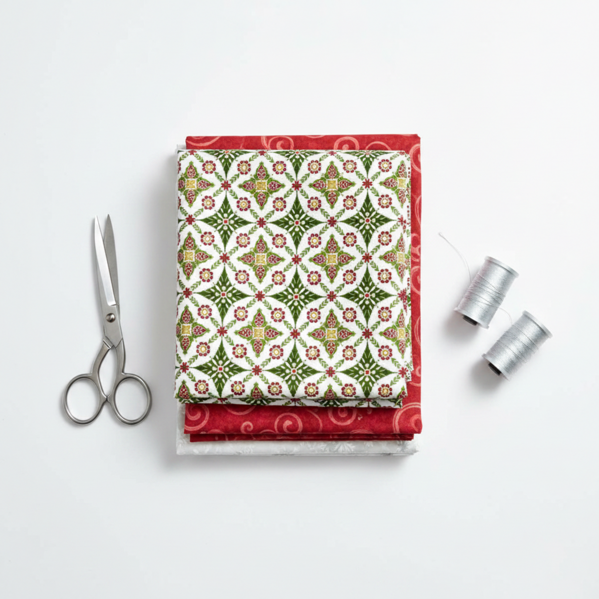 NYSNO New Snow Multicolor Garland quilting cotton by Jason Yenter for In The Beginning Fabrics — folded as hero on a coordinating stack Red Swirl and White Snowflakes, silver scissors and thread spools on white surface. Coordinating fabrics and quilt patterns available at IraRobi Quilts.