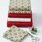 NYSNO New Snow Multicolor Garland quilting cotton by Jason Yenter for In The Beginning Fabrics — vertical flat lay folded as hero on a tall coordinating stack with NYSNO Red Swirl and White Snowflakes, silver scissors and thread spools to the side. Coordinating fabrics and quilt patterns available at IraRobi Quilts.