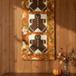 Oh Snap! gingerbread wall hanging by Jennie Jo Lamb for Lamb Farm Designs — three gingerbread person appliqué blocks with ric-rac trim on cream backgrounds, bordered by Autumn Celebration Multi Circles fabric by Jason Yenter with large medallion circles in crimson, orange, and golden yellow autumn leaves. Displayed on a rustic wood-paneled wall above a sideboard styled with a pumpkin and fall berry branches. Quilts shown for inspiration feature the Oh Snap! pattern by Jennie Jo Lamb — available at IraRobi Q