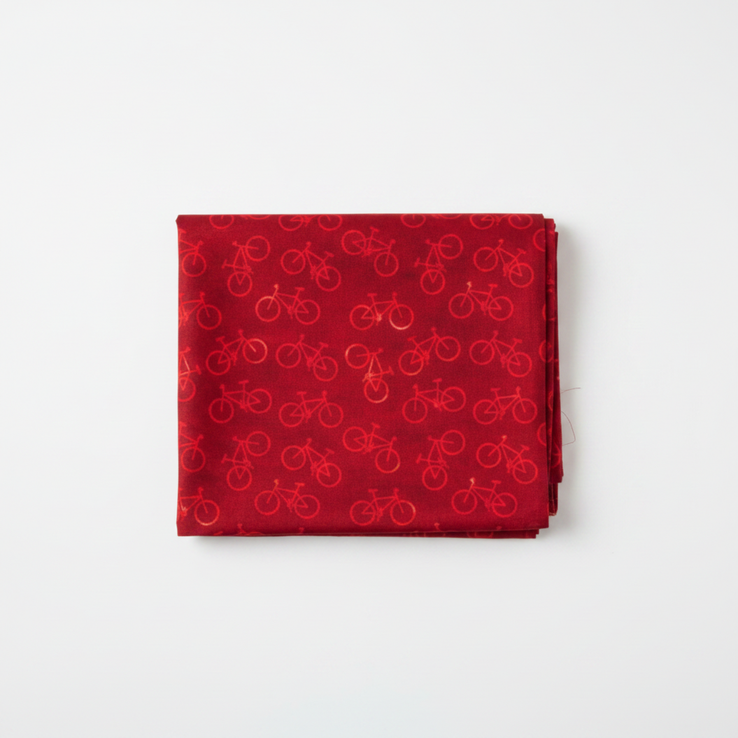 On the Go Bicycles Red quilting cotton by Jason Yenter for In The Beginning Fabrics — folded yardage on a white surface showing scattered tone-on-tone road bicycle silhouettes in warm crimson on a deep red mottled ground, selvage edge visible at right, 100% cotton, 43–44" wide.