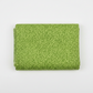 On the Go Leaves Green quilting cotton by Jason Yenter for In The Beginning Fabrics — folded yardage on a white surface showing the dense tone-on-tone leaf print in soft chartreuse-green on a lush grass-green ground, raw selvage edge visible at left, 100% cotton, 43–44" wide.