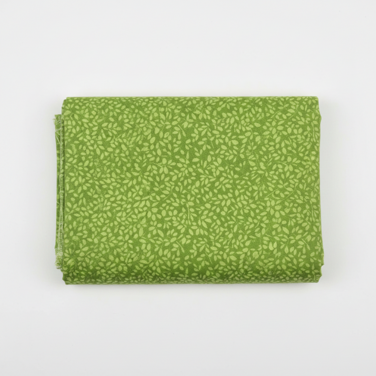On the Go Leaves Green quilting cotton by Jason Yenter for In The Beginning Fabrics — folded yardage on a white surface showing the dense tone-on-tone leaf print in soft chartreuse-green on a lush grass-green ground, raw selvage edge visible at left, 100% cotton, 43–44" wide.